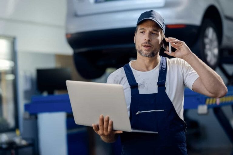 auto repairman talking on the phone while using laptop in a workshop